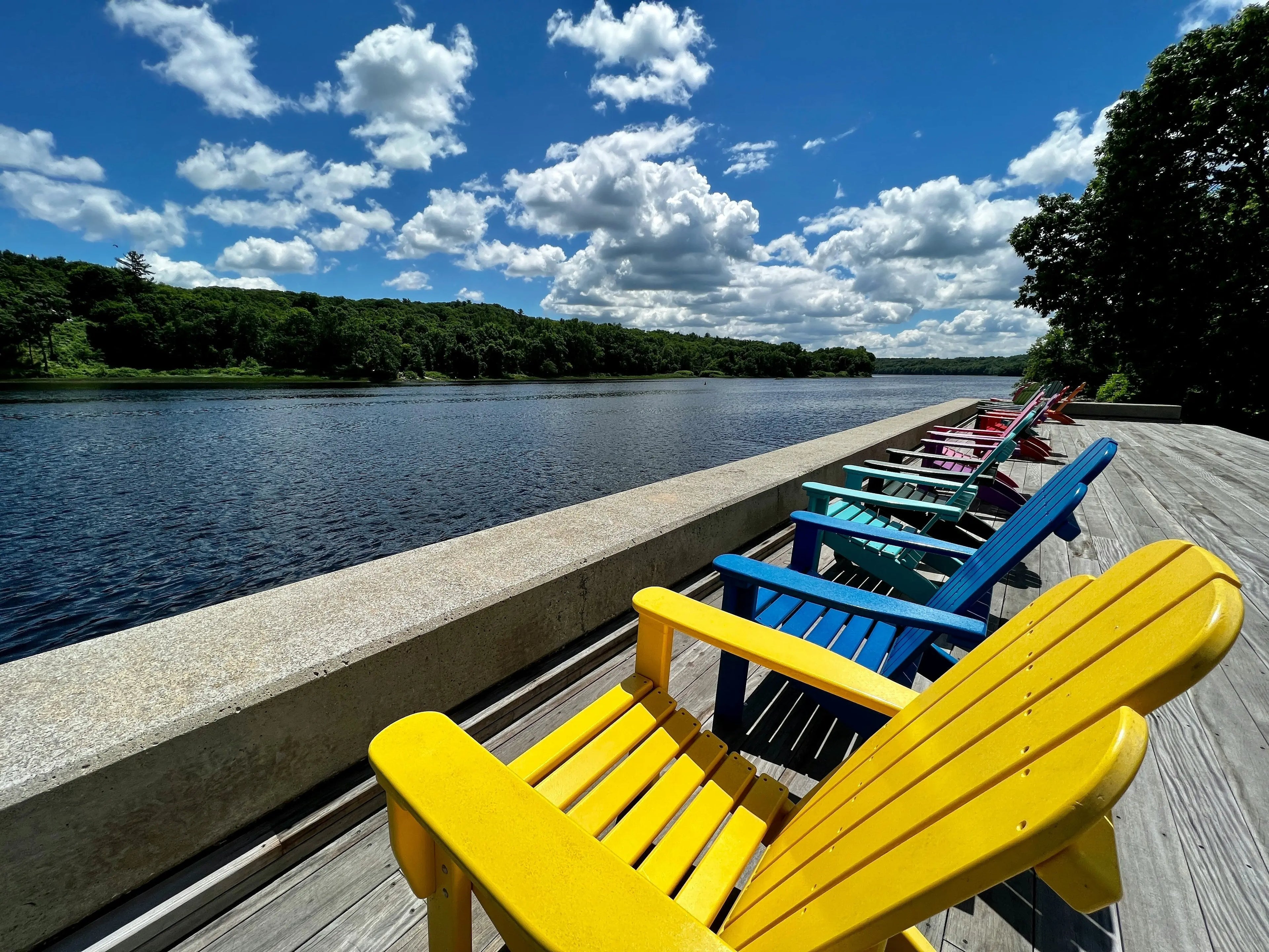 Fauteuils de jardin Adirondack colorés alignés au bord d'un lac sous un grand soleil